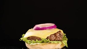 A slow-motion sequence shows a tomato slice and sesame seed bun top falling onto a beef burger with cheese, lettuce, and onion against a black background - Powered by Shutterstock - Get 15% off with code: PIKWIZARD15