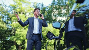 Stressed professional businessman, dressed in a grey suit, makes an urgent phone call outdoors beside a charging electric vehicle. Expresses frustration and concern during conversation. - Powered by Shutterstock - Get 15% off with code: PIKWIZARD15