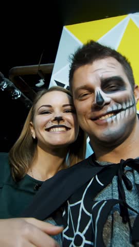 Halloween party, night, frightening portrait of a man with a terrible makeup in a black costume and a girl in a cat costume, they croak in front of the camera