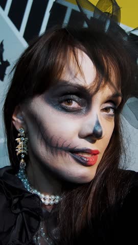 Halloween party, night, frightening portrait of a woman with a terrible makeup in a black witch suit, croaks in front of the camera