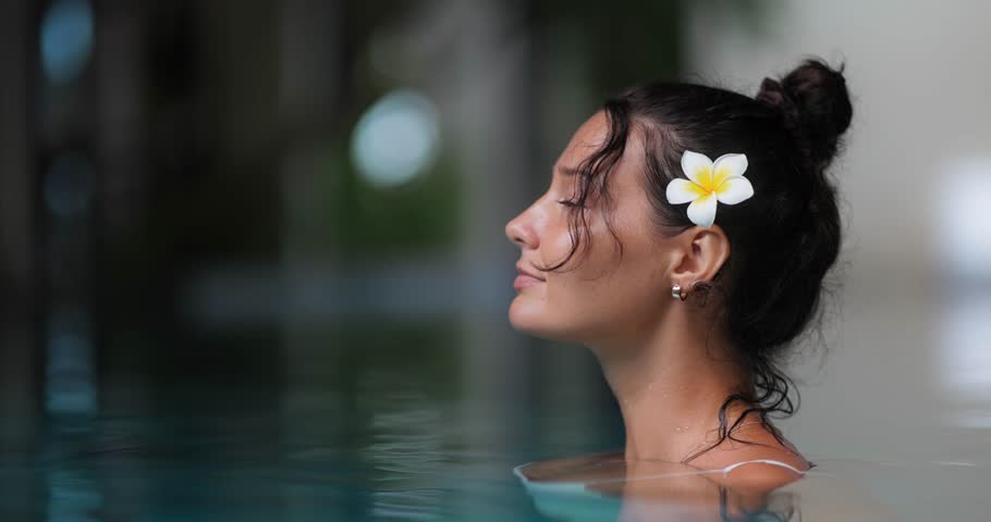 Elegant young woman standing still in water with eyes closed and flower in hair, enjoying peaceful spa moment. Perfect for luxury wellness, skincare, travel and lifestyle concepts.