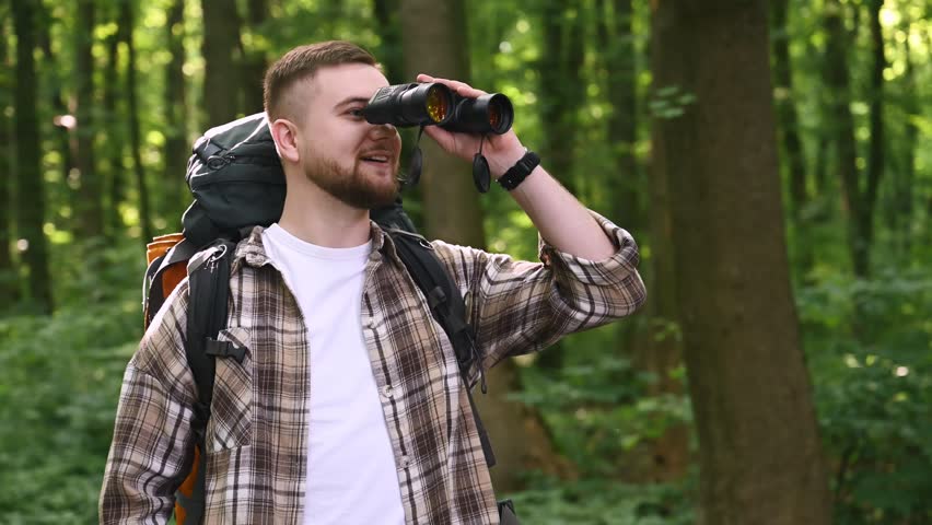 Using binoculars. Male tourist is with backpack in the forest.
