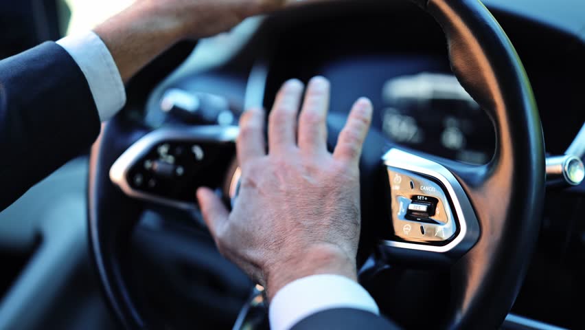 Professional businessman inside a modern car, dressed in a dark suit, impatiently honking the car horn. His actions convey frustration while driving during traffic.