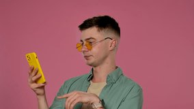 A man wearing yellow sunglasses scrolls through the feed on his smartphone and wonders at the pink background, creating a stylish and fashionable studio atmosphere. - Powered by Shutterstock - Get 15% off with code: PIKWIZARD15
