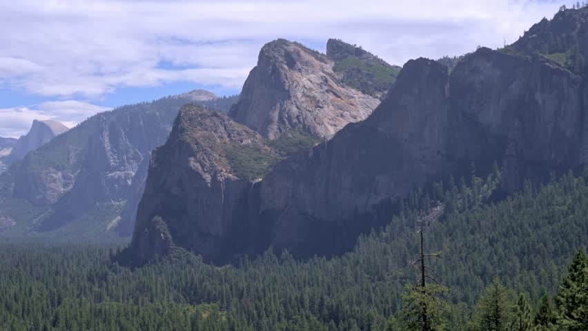 Footage showcasing the stunning Bridalveil Falls alongside the iconic Three Brothers granite rock formation in Yosemite National Park, California.