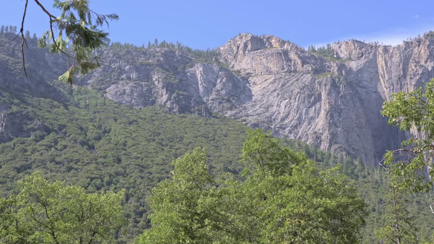 Editorial footage of a panoramic pan across the granite cliffs of Yosemite National Park in California, featuring the towering presence of El Capitan.