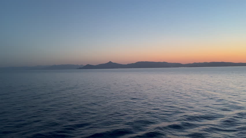 Calm twilight water off the coast of an Island in the Saronic Gulf with gentle waves reflecting golden hour light.