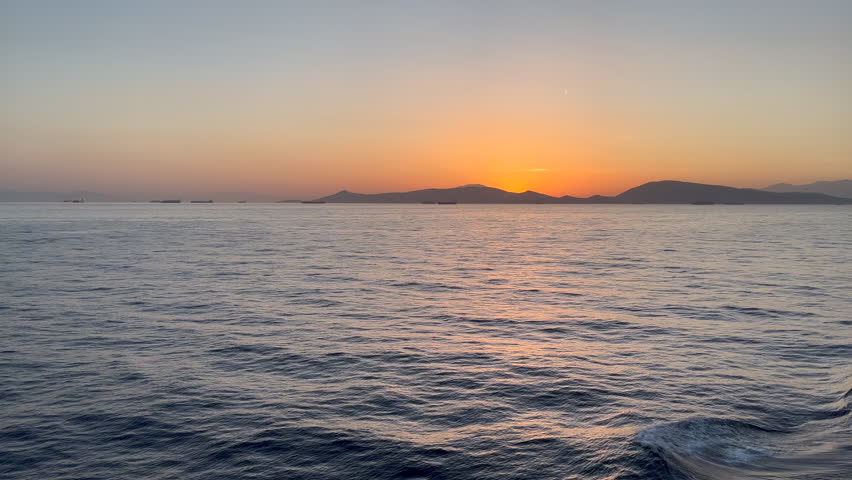 Calm twilight water off the coast of Salamina Island with gentle waves reflecting golden hour light off the coast of Greece.