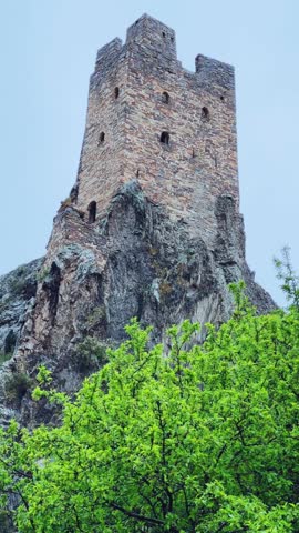 The tower complex is located inside the green mountains. The Republic of Ingushetia, Russia. View of the defensive towers of Ingushetia in the North Caucasus on a cloudy day in spring. 4K
