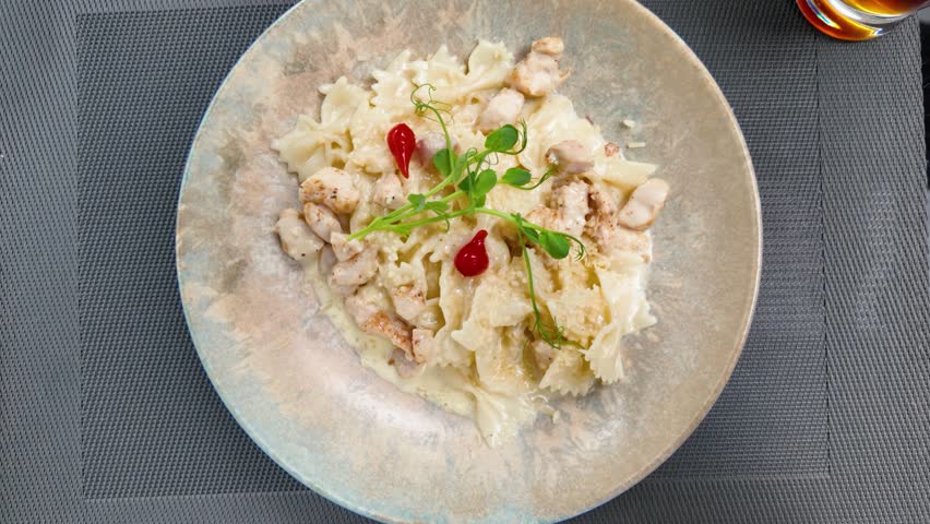 Delicious creamy farfalle pasta with chicken, parmesan, microgreens, and red peppers served on a rustic plate in a modern restaurant setting, top view