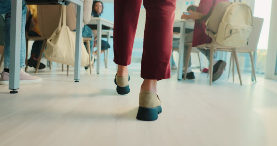 Legs, person and teacher walking in classroom to monitor students, exam supervision and protocol. Feet, lecturer and invigilation of assessment, prevent cheating and maintain order of time management