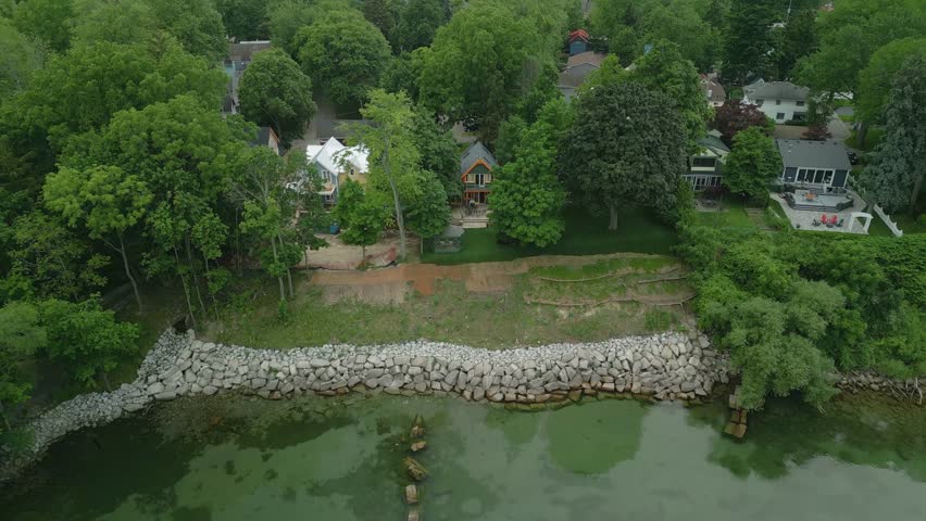 A drone view of Lakeside homes nestled among trees face a rocky shoreline, with grassy terraces leading to the calm water