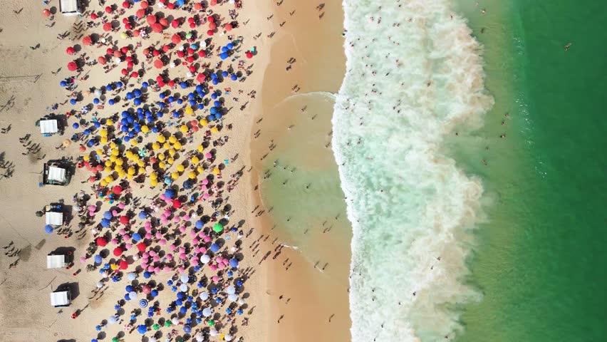 Top-down drone view of Copacabana’s colorful umbrellas and surf along Rio’s sunny coastline
