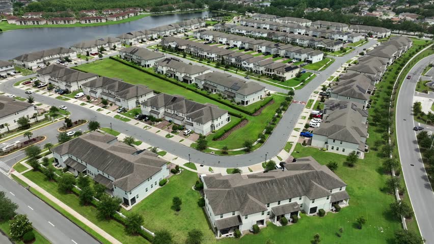 Luxury row of houses near lake in suburb neighborhood of Orlando, Florida. Aerial wide shot. White apartment houses with grey roof in modern style. Upscale housing area of American city.