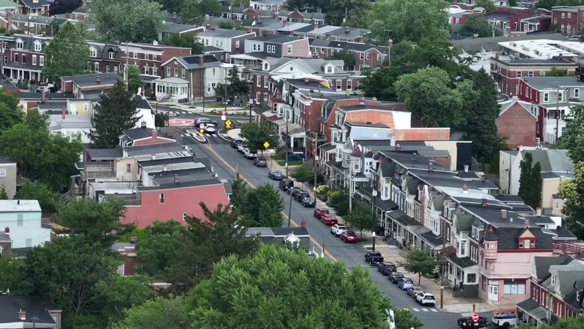 Aerial view of Lancaster, PA neighborhood with historic brick row houses, tree-lined streets, and parked cars. Charming small-town American architecture in a peaceful residential area. Wide shot.