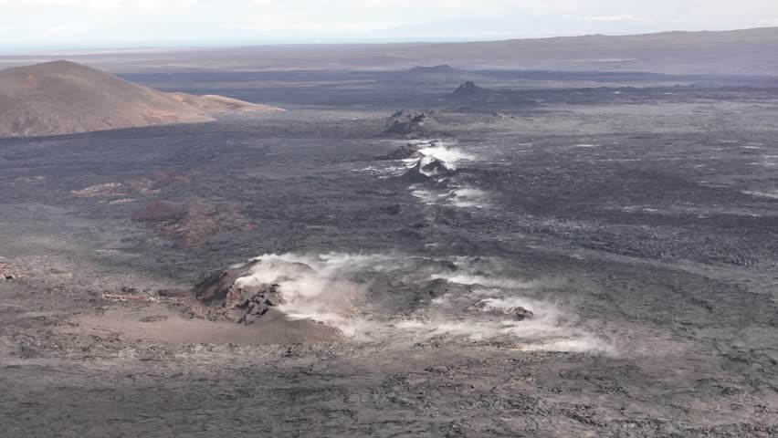 Aerial view of Icelandic volcanic terrain with multiple steam vents and blackened lava fields stretching across the landscape.