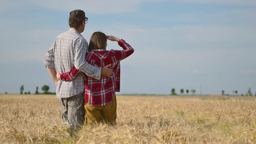 Male and female farm workers posing in ripe wheat plantation field ready for harvest, 4K with selective focus