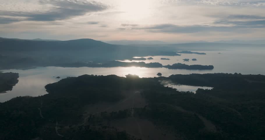 Aerial view of a Lake Alumine reflecting the sunlight and surrounded by forested hills and distant mountains under a dramatic cloudy sky. Villa Pehuenia, Neuquen, Patagonia, Argentina