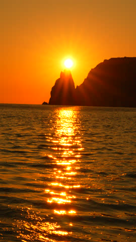 Sunset, ocean, water golden light path over sea with setting sun behind cliff. Vertical video