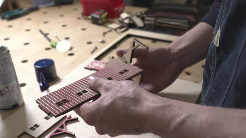 the worker laser cuts out parts of wood, makes a roof from an aluminum can, paints and patinas the future walls, glues everything together into one structure and the result is a miniature farmhouse