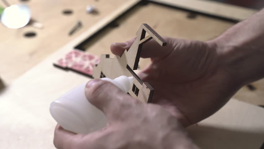 the worker laser cuts out parts of wood, makes a roof from an aluminum can, paints and patinas the future walls, glues everything together into one structure and the result is a miniature farmhouse