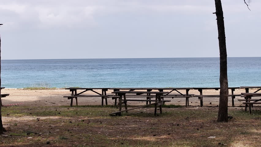 A tranquil beach scene with picnic tables under trees, overlooking the calm waters in Kusadasi, Turkey, oe01