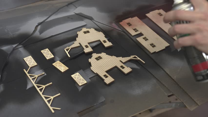 the worker laser cuts out parts of wood, makes a roof from an aluminum can, paints and patinas the future walls, glues everything together into one structure and the result is a miniature farmhouse