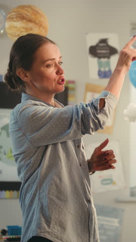 STEM Class: Female Teacher Teaching Environmental Science to Elementary School Kids in Modern Classroom. School Girl Presenting Renewable Energy Sources Using Model of Earth. Dolly Shot. Vertical Shot