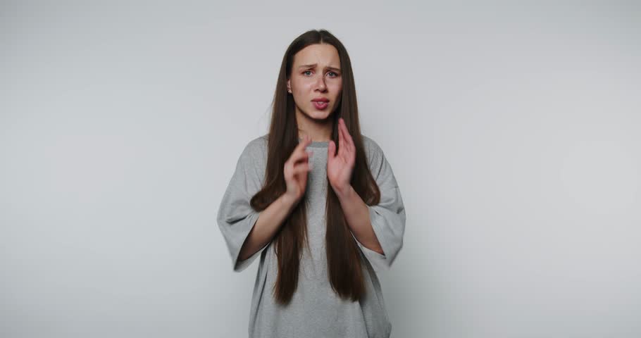 Young woman expressing fear while holding hands to her face in a minimalist studio setting