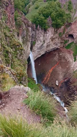 The powerful waterfalls flow gracefully down the steep cliffs, surrounded by vibrant green hills and rocky outcrops. Nature