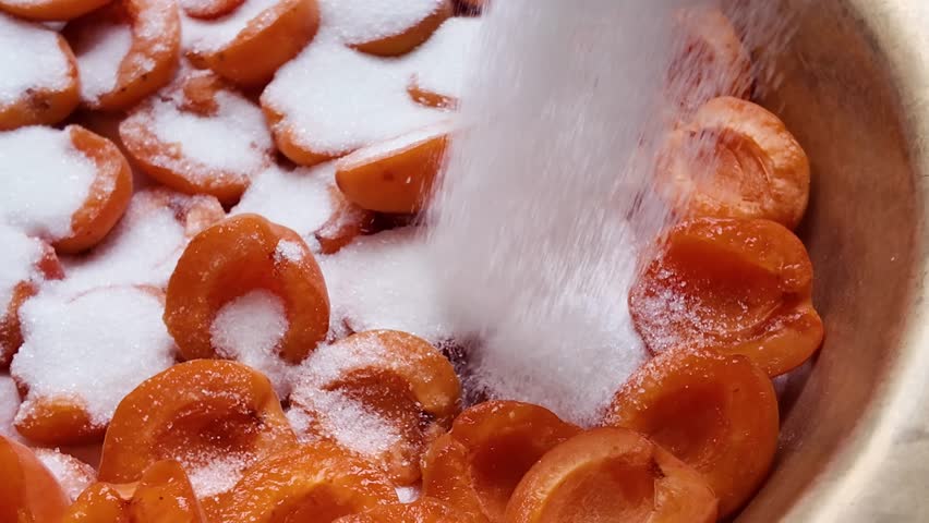 Apricot slices in a copper bowl are sprinkled with sugar during the preparation of apricot jam