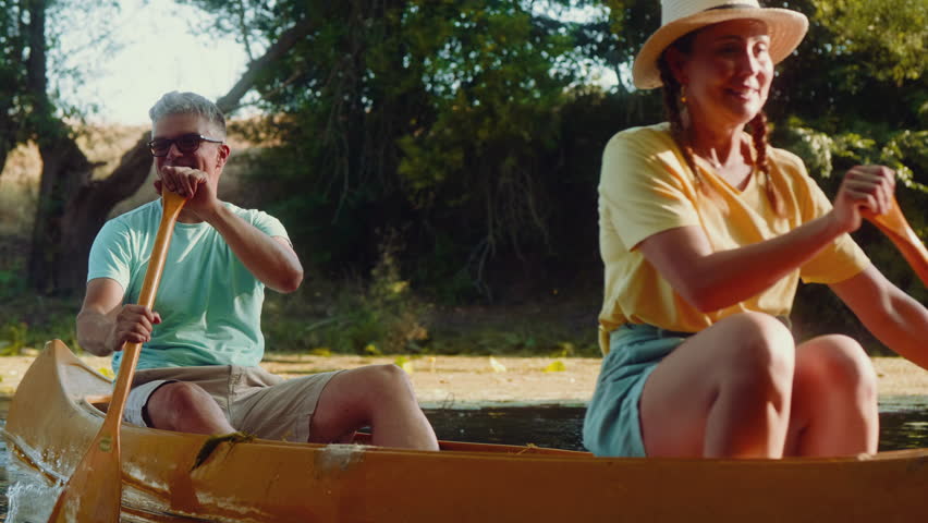 A depiction of a smiling, middle-aged couple enjoying a canoe ride on a serene river, exploring untouched nature