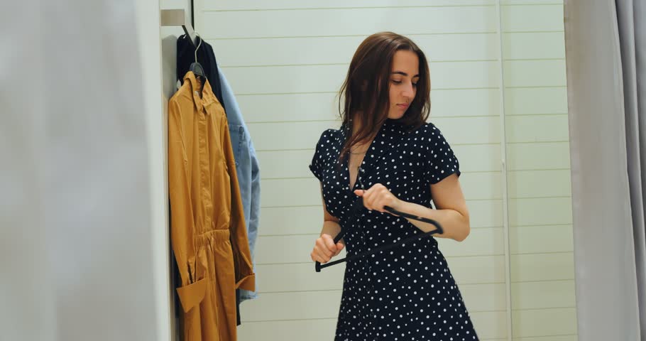 Woman spinning in fitting room showing off new outfit, spin gesture repeated to emphasize dress flow, mirror image framing energetic wardrobe exploration moment with upbeat styling vibe