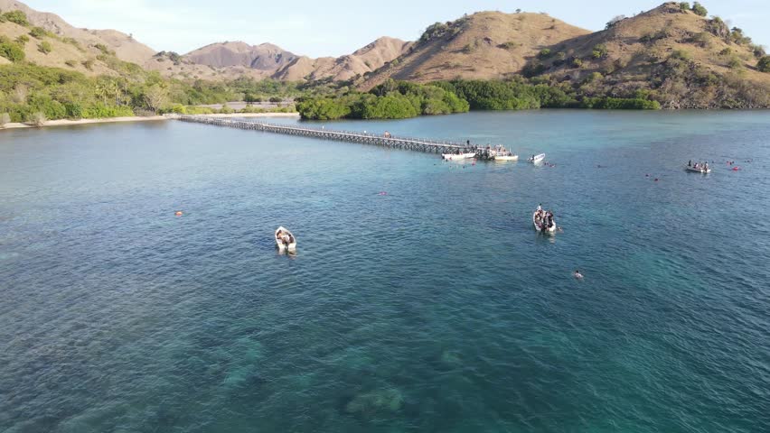 Aerial view of beach with long bridge and tourist boat sailing in Manjarite Island, Indonesia.