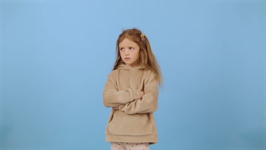 Young girl with crossed arms shows displeasure in a studio setting with a light blue background
