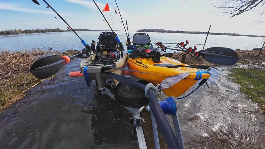 Fishing kayaks prepared for the launch and fishing at the lake. Boat trailer at the ramp water access attached to the truck hitch mount and fishing pedal kayaks. Sport fish tournament at spring.