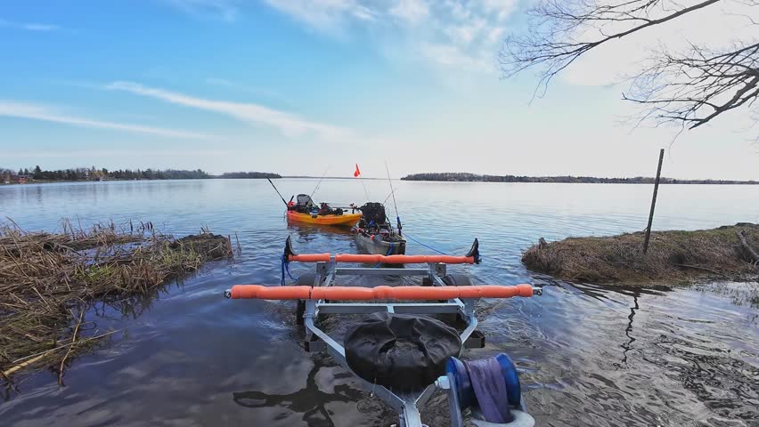 Fishing kayaks prepared for the launch and fishing at the lake. Boat trailer at the ramp water access attached to the truck hitch mount and fishing pedal kayaks. Sport fish tournament at spring.