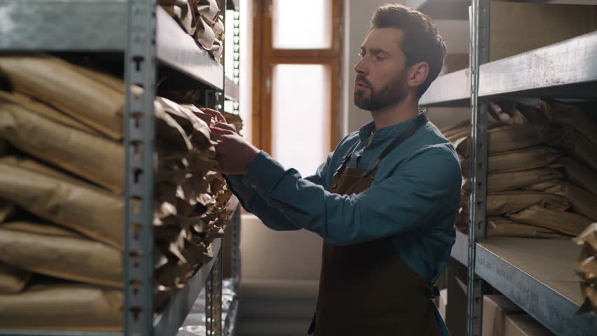 Professional Caucasian man barista coffee warehouse worker searching storage shelf bag beans male small business owner apron production espresso inventory packaging caffeine arabica robusta industry