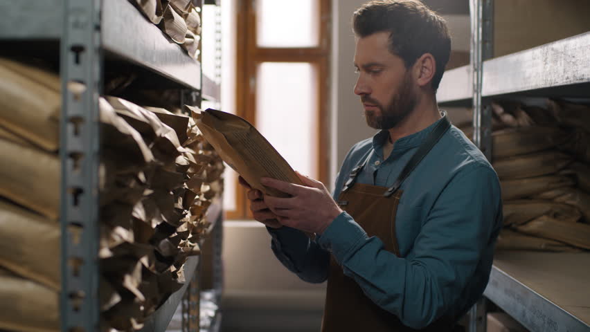 Professional Caucasian man barista coffee warehouse worker searching storage shelf bag beans male small business owner apron production espresso inventory packaging caffeine arabica robusta industry