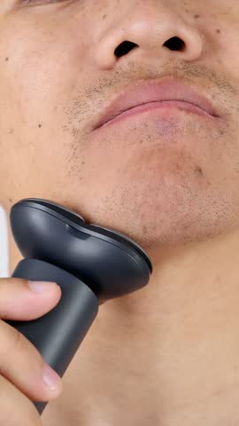 closeup of Asian man shaving with an electric shaver