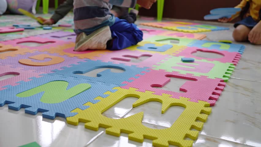 Unrecognizable children placing foam letters into a colorful alphabet puzzle mat on the floor. Preschool literacy activity supports letter recognition and fine motor skill development in kindergarten - Powered by Shutterstock - Get 15% off with code: PIKWIZARD15