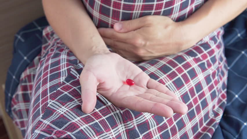 Closeup view of opening female palm with a red pill. Woman is holding her stomach. She feels pain, and intends to take painkiller. Pharmacy and health care concept. Pill in female hand.
