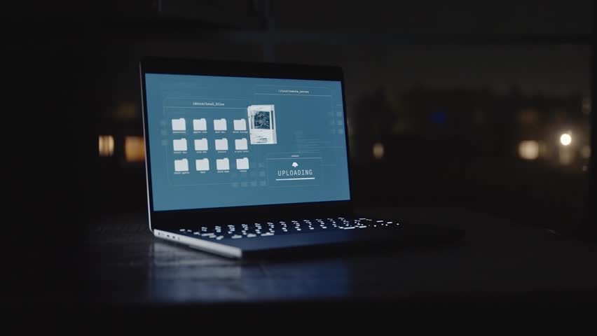 Laptop computer of office desk at night with secret files uploading to server. Remote access of government archive and data information. Classified files transfer to cyber cloud by hacker or spy