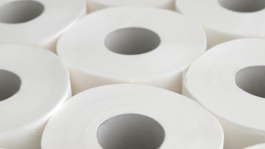 Camera pans over soft-lit toilet paper rolls in close-up on bathroom surface, for hygiene product promo