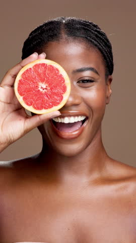 Skincare, grapefruit and face of black woman in studio with natural, organic or cosmetic routine. Portrait, dermatology and African person with citrus fruit for facial brightening by brown background