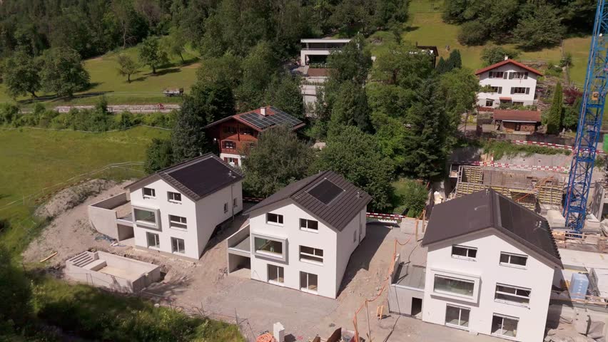 Single family houses in swiss town during building phase. Construction site with crane in alps mountains. Sunny day sin summer. Aerial backwards shot.