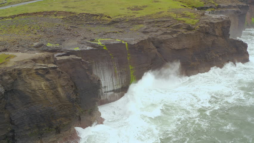 Aerial dynamic shot captures the sharp edges of the Cliffs of Moher battered by a rough Atlantic Ocean. Doolin