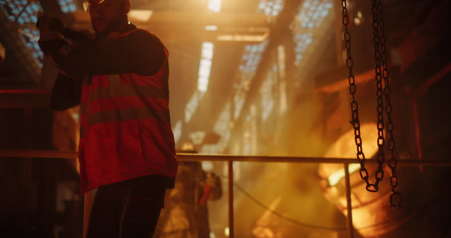 Smelter Operators in Protective Fireproof Suits and Industrial Employees Working at a Modern Metal Foundry. Foundrymen Pouring Hot Melted Iron Ore into Casting Forms, Producing Equipment