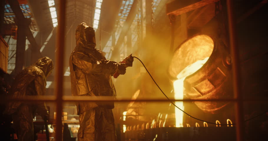 Smelter Operators in Protective Fireproof Suits and Industrial Employees Working at a Modern Metal Foundry. Foundrymen Pouring Hot Melted Iron Ore into Casting Forms, Producing Equipment