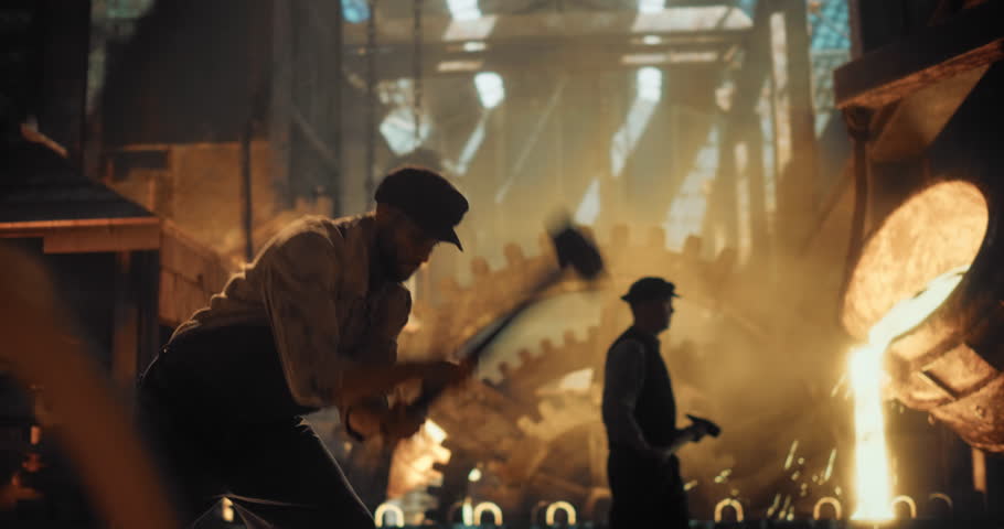 Man in Worn Work Clothes Strikes Iron with a Sledgehammer Inside a Gritty, Fire-Lit Workshop. Man s Doing Manual Labor During the Industrial Revolution. Cinematic Slow Motion Footage